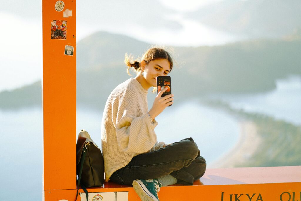 Young woman sitting at Likya Observation Point, capturing the serene landscape with her phone.